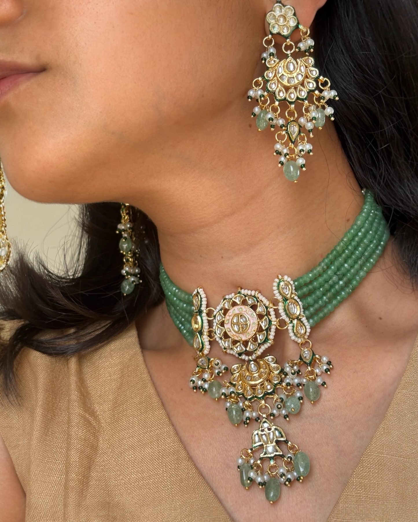 Close-up of a woman wearing a green and gold necklace with matching earrings.