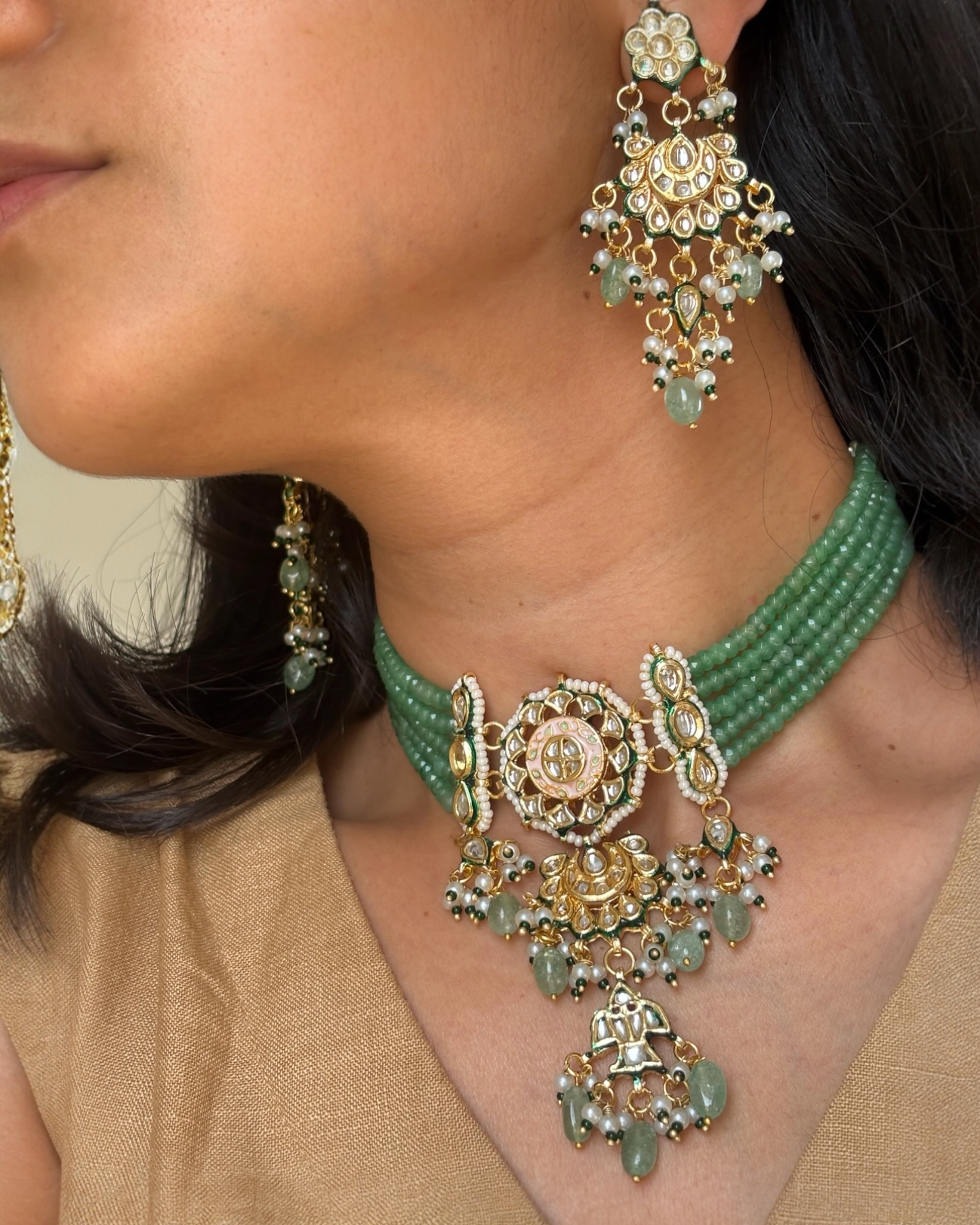 Close-up of a woman wearing a green and gold necklace with matching earrings.