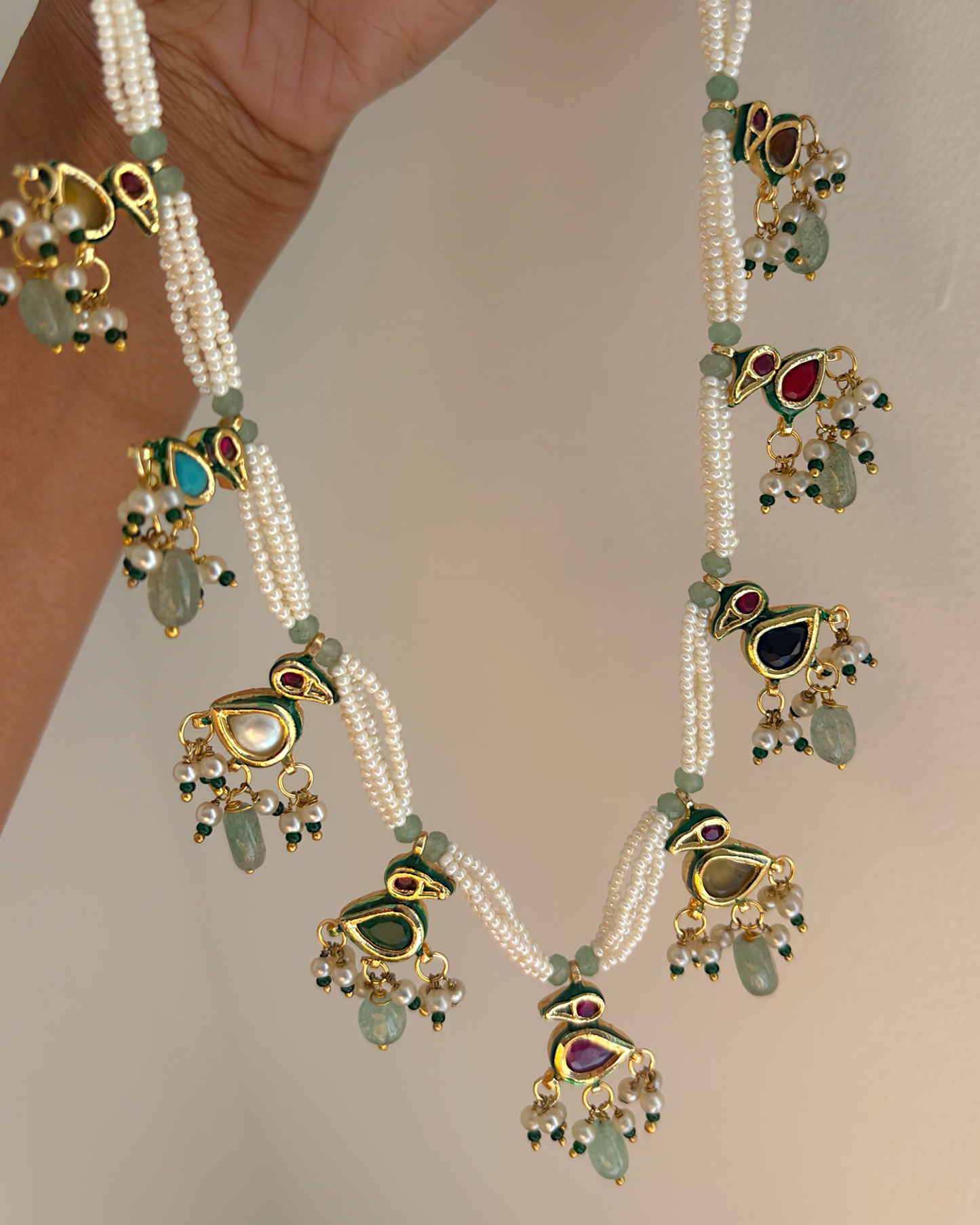 Delicate necklace with green and gold pendants on a plain background